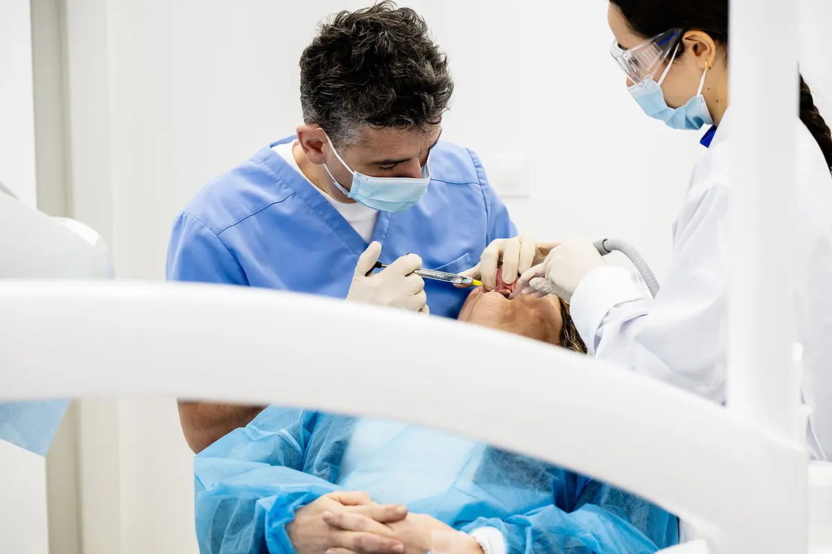 Un chirurgien et son assistante au fauteuil, les mains du patient croisées
